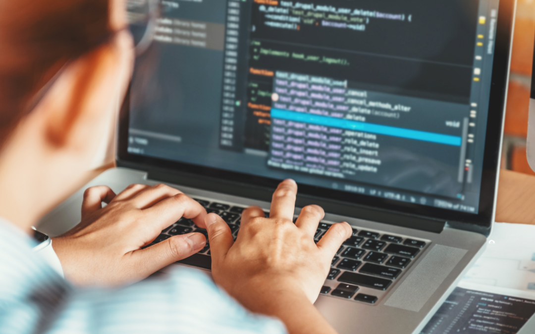 A woman typing on a keyboard on her laptop. On the screen are lines of code.