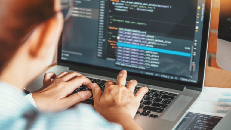 A woman typing on a keyboard on her laptop. On the screen are lines of code.