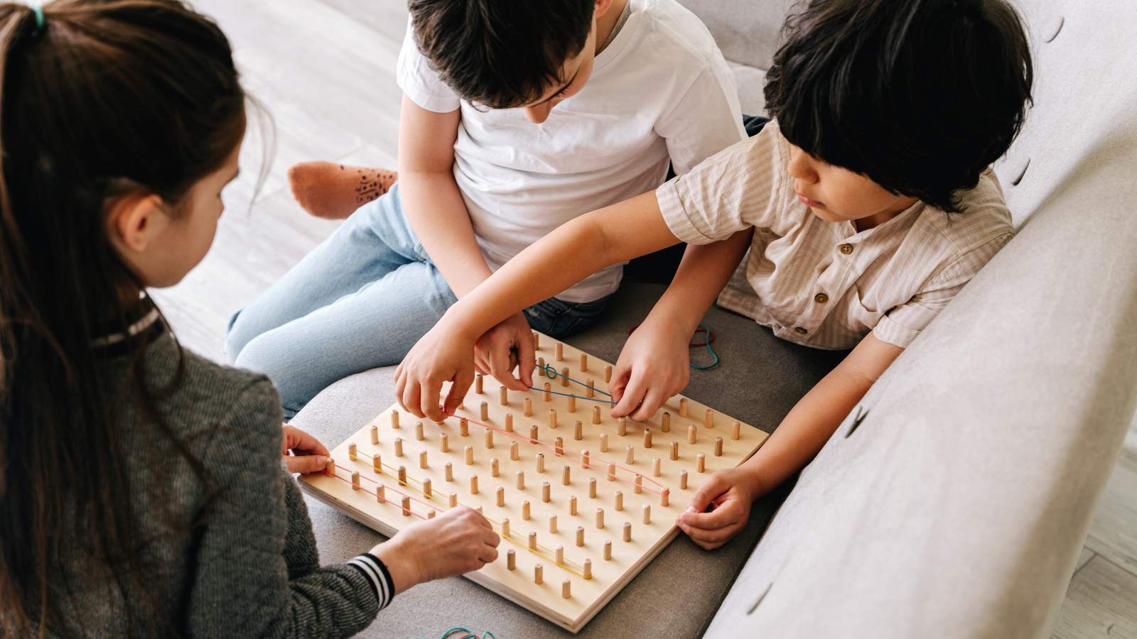 Two boys play a boardgame on the couch with a girl