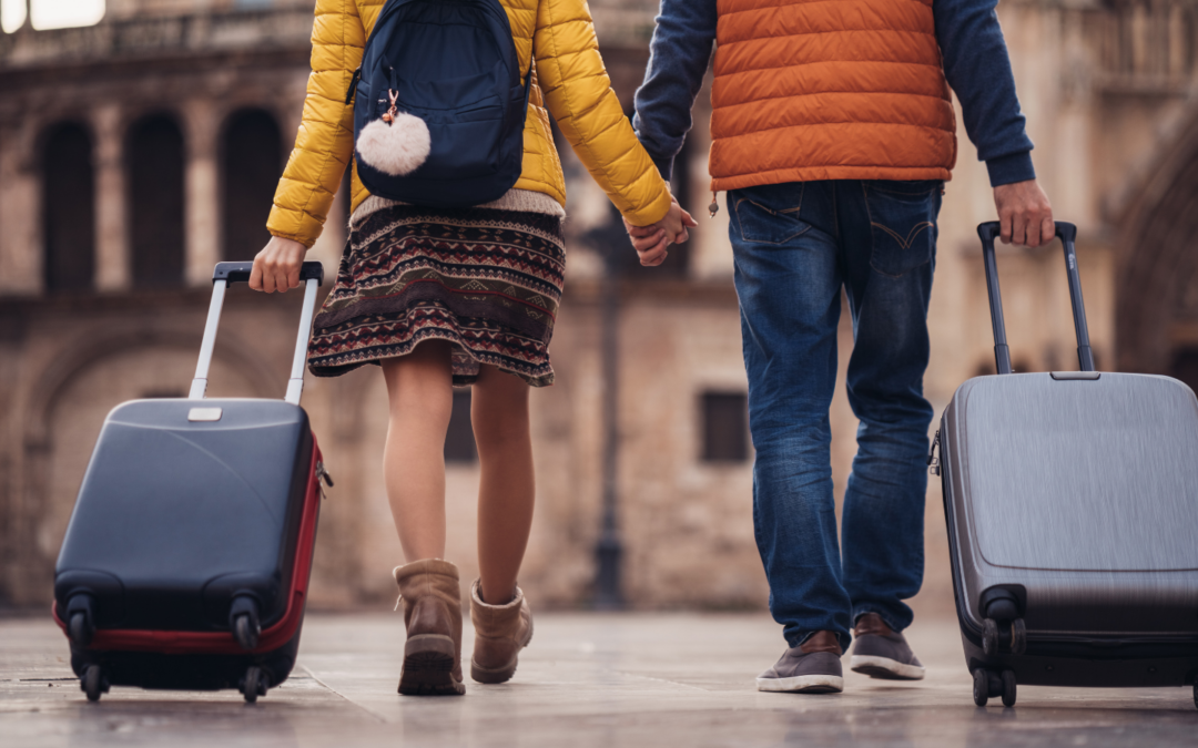 Two tourists holding hands and wheeling suitcases.